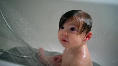 Bebek, gün ışığında banyo yaparken tuhaf bir keşif ve şefkat ifadesi ile duşun altına bakıyor.