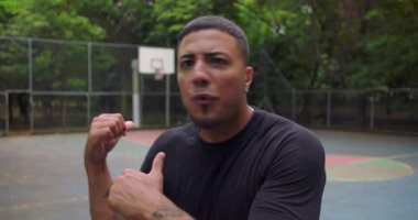 Açık hava basketbol sahasında kızgın bir şekilde bağıran ve kameraya doğru hareket eden Afrikalı Amerikalı bir adam, yoğun duygusal çatışmalar, POV perspektifi