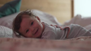 Yumuşak yatakta uzanan bebek, ılık bir sabah ışığında hafifçe gülümsüyor. Huzurlu bir evde masumiyet ve şefkat ifade ediyor.