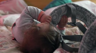 Bebek yatakta kayışı tutuyor, rahat bir şekilde uzanıyor çiçek çarşafları ve yastıklarla, yumuşak merakla dokuları keşfediyor.