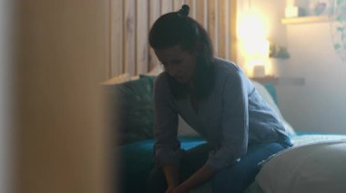 Kadın loş yatak odasında oturuyor, düşünceli bir ifadeyle öne eğiliyor, duygusal yorgunluk ve yalnızlık, zihinsel yorgunluk ve sessiz yansıma anı