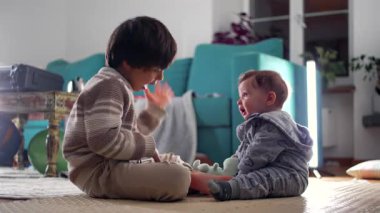 Ağabeyim neşe içinde başını sallayarak bebeği güldürüyor, neşeli kardeş etkileşimi kahkahalarla, şefkatle ve sıcak aile oturma odasında.