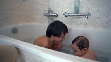 Ağabey, bebek kardeşiyle banyo sırasında etkileşime geçiyor. Evdeki çocuklar arasında merak, şefkat ve bağ gösteren şefkatli ve neşeli bir aile anı.