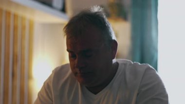 Orta yaşlı bir adam, elleri alnında yatakta oturuyor, inanmazlık ve pişmanlık içinde başını sallıyor, duygusal acı, keder ve samimi aile ortamında kendini kınıyor.