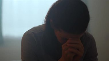 Yatakta başı eğik ve elleri bağlı bir kadın, derin bir düşünce ve duygusal mücadele içinde, stres, keder ve kırılganlık anını temsil ediyor.