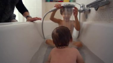 Ağabeyi küvette duş alan bebek kardeşi gözetim altında, neşeli ve şefkatli aile anı evde akşam rutini sırasında şefkat, şefkat ve yakınlık gösteriyor.