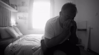 Yatakta oturan bir adam iki eliyle yüzünü kapatıyor. Kederin, yorgunluğun ve umutsuzluğun sessiz anlarında çaresizlik ve duygusal çöküntü gösteriyor.