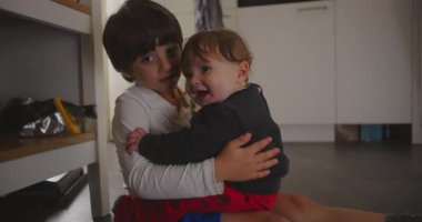 Ağabeyi mutfakta oturmuş bebeğini kucağında tutuyor, hafifçe gülümsüyor, sıcaklığını, sevgisini ve evdeki aile sevgisinin hassas duygusal bağlantısını gösteriyor.