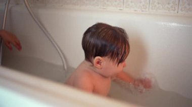 Küçük çocuk klasik banyoda banyo yapıyor, yumuşak doğal ışık altında suda sessizce oynuyor, masumiyetini, hijyenini ve günlük rutinini gösteren huzurlu çocukluk anı..