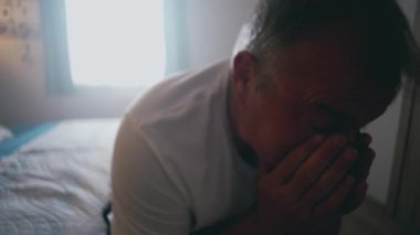 Yüzü ellere gömülmüş bir adam, derin bir üzüntü, stres ve umutsuzluğu ifade ederek derin bir ev ortamında.