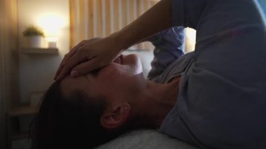 Yatakta uzanmış elleri loş yatak odasında uzanmış bir kadın, yorgunluk ve duygusal yansıma, yalnızlık ve stres atağı.