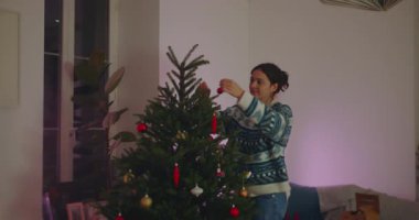 Annem Noel ağacını rahat oturma odasında süsledi, bayram döneminde şenlikli bir kutlamaya hazırlanıyor, sevinç, sıcaklık ve huzurlu aile atmosferini ifade ediyor.