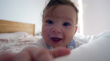Bebek yatağında uzanmış, neşeli bir ifadeyle doğrudan kameraya bakıyor. Parlak, samimi yatak odası ortamında samimiyet ve bağlılık gösteriyor.