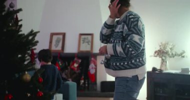 Annem Noel ağacını süs eşyalarıyla süslerken çocuk gözetliyor, sıcaklığını, aile beraberliğini ve evde tatil hazırlıkları sırasında şenlik ruhunu ifade ediyor.