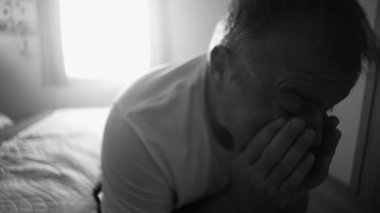 Adam iki eliyle yüzünü kapayarak yatakta oturuyor. Siyah ve beyazdaki hüzün ve zihinsel mücadele sırasında duygusal acı, yorgunluk ve çaresizlik ifade ediyor.