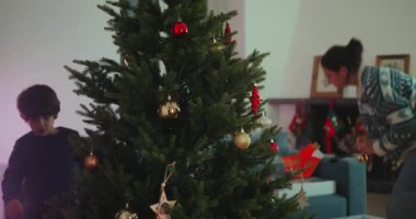 Anne ve oğul Noel ağacını evde birlikte süslüyor, sıcaklığı ve neşeyi paylaşıyor, aile sevgisini, bağlılığı ve tatil sezonunun ruhunu ifade ediyor.