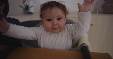 Bebek yüksek bir sandalyede oturuyor, kollarını açıp gülümsüyor, neşeyle ve merakla gülüyor, masumiyeti, sıcaklığı ve çocukluk yıllarının neşeli enerjisini yakalıyor..