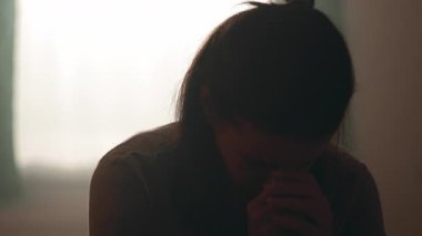 Sabahın yumuşak ışığında tek başına oturan kadın, ellerini sımsıkı tutarak derin üzüntüsünü, yorgunluğunu ve samimi bir yuva kurmak için verdiği çabayı ifade ediyor.