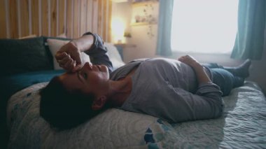 Yatak odasında uzanmış bir kadın, elleri alnında dinleniyor. Yorgunluk sembolü, duygusal gerginlik ve evde yorgunluktan sonra sessizce iyileşme.