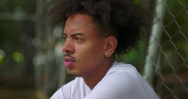 Basketbol sahasında oturan Afrikalı bir gencin yan görünüşü. Dışarıdaki sakin ortamda yansıma, azim ve umudun ifadesi.