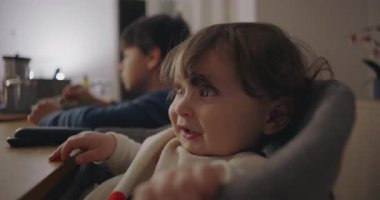 Küçük çocuk yemek saatinde yüksek sandalyede oturuyor. Ailelerine uzanıyor ve onlarla iletişim kuruyor. Evde her gün neşe ve özgün çocukluk anları yaşanıyor..