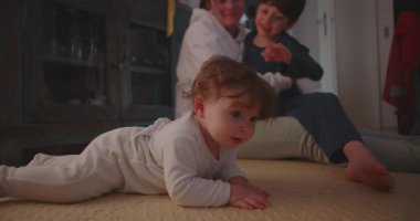 Çocuk yerde yatarken, anne ve kardeşinin etkileşim halindeyken, aile bakımını, erken keşifleri ve çocukluk anılarını görürken, meraklı bir bakışla yerde yatıyor.