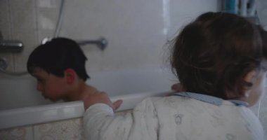 Yavru bebek küvetin yanında durmuş ağabeyini izliyor. Evde banyo yaparken kardeş meraklısı masumiyetini ve aile anını gösteriyor..