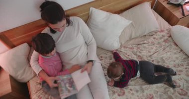 Anne yatakta oğluna kitap okurken bebek onların yanında yatar. Huzurlu bir evcil an anne sevgisini, sıcaklığını ve sıcacık yuva ortamındaki bağlantısını ifade eder.