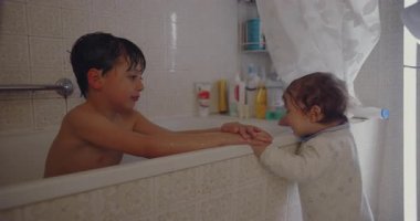 Ağabeyim, küvetin yanında bebek bebekle oynuyor. Banyo zamanı, kardeş neşe dolu etkileşimleri ve aile bağlarını gösteriyor..