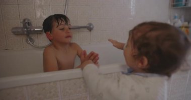 Ağabeyi küvette gülümserken, küçük bebek evde her gün banyo yaparken neşeli kardeş bağları ve aile bağlarını göstermek için elini uzatıyor..