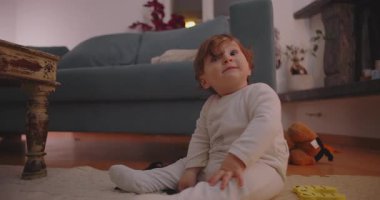 Küçük çocuk kanepe ve oyuncakların yanında oturmuş, düşünceli bir ifadeyle yukarıya bakıyor, çocukluğunda merak, merak ve hayal gücünü gösteriyor..