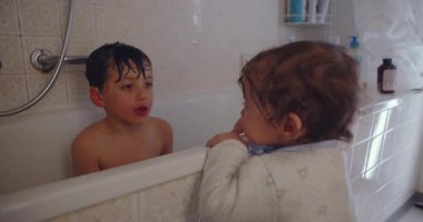 Bebek bebek, küvette ağabeyini öpmek için eğiliyor. Banyo sırasında neşeli bir sevgi gösterisi yapıyor. Kardeş bağı ve evde şefkatli aile sevgisini gösteriyor..