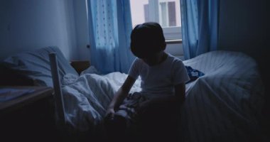 Başı eğik, karanlık bir odada tek başına oturan çocuk üzüntüyü, yalnızlığı ve çocukluk depresyonunu simgeliyor.