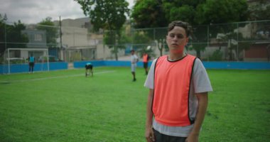 Latin Latin asıllı bir adam futbol sahasında turuncu eğitim yeleği giyiyor, ciddi ve kendinden emin görünüyor, açık hava antrenmanlarında kararlılığını ve odaklanmasını ifade ediyor.