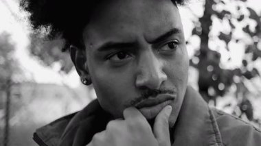 Afrika kökenli genç adam yakından düşünceli bir ifade içinde, dışarı bakarken el pençe üzerinde dinleniyor, ciddi ve içsel duygusal portre, siyah ve beyaz