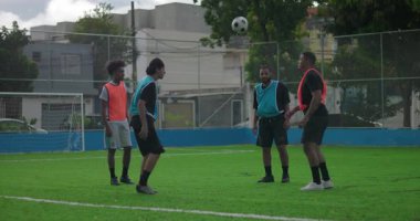 Sahada futbol paslaşması yapan, top kontrolü ve iletişimine odaklanan dört adam, açık hava dostluk maçından önce birlik, disiplin ve takım çalışmasını ifade ediyorlar.