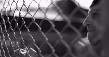 Hispanik adam öfke ve hüsran içinde çitlere çarpıyor, ham duygular ve iç karışıklığı ifade ediyor cesur siyah ve beyaz sahnede