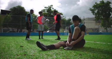 Arkadaşlarıyla gündelik futbol maçından önce ayakkabı bağı bağlayan genç İspanyol bir adam sahada onlara katılmak için ayağa kalkıyor takım çalışması, hazırlık, dostluk ve oyun hevesini gösteriyor.