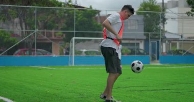 Antrenman sırasında futbol sahasında tekme atan genç adam, şehir parkında odaklanma ve hassasiyetle futbol topunu kontrol ediyor, yetenek, denge ve koordinasyon gösteriyor.