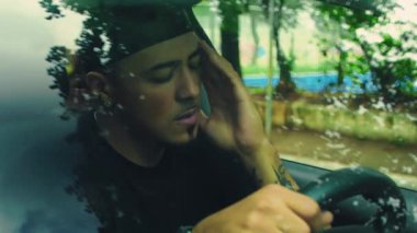 Adam direksiyona yaslanmış bir şekilde öne doğru eğiliyor, arabanın içindeki stresli anlarda yorgunluk, umutsuzluk ve sessiz duygusal çöküntü taşıyor.