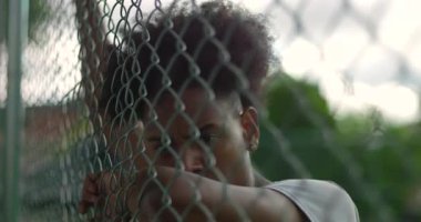 Çitin arkasındaki genç Afrikalı Amerikalı adamın yakın çekimi duygusal gerginlik, yorgunluk ve mücadele üstüne direnç gösteriyor.