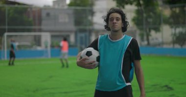 Antrenman sırasında futbol topu tutan İspanyol bir adam, sakin ve kendinden emin ifade maç öncesi hazırlık ve kararlılığı simgeliyor