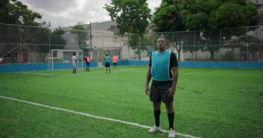 Latin kökenli, Afrika kökenli, takım arkadaşları, takım çalışmasının, gururun ve kararlılığın sembolü olarak arka planda bulanık bir şekilde futbol sahasında güvenle duran Latin asıllı bir adam.