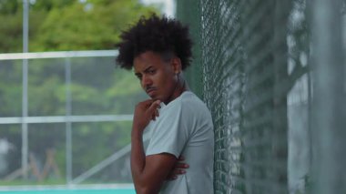 Afrika kökenli Amerikalı bir adam, tel örgülere yaslanmış, düşünceli ve dalgın görünüyor, elleri çenesinde, şüphe, yansıma ve sessiz düşüncelerini dışa vuruyor.