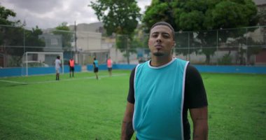 Latin futbolcu şehir sahasında kendinden emin görünüyor, maçtan sonra kolları gevşemiş, takım arkadaşları mesafeyi görüyor, gurur kavramı, takım çalışması ve sporda azim.