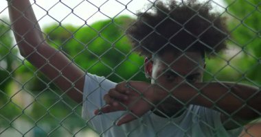 Genç Afrikalı Amerikalı adam, yorgun ve düşünceli bir şekilde çitin üzerinde dinleniyor. Duygusal yorgunluk ve iç mücadele gösteriyor.