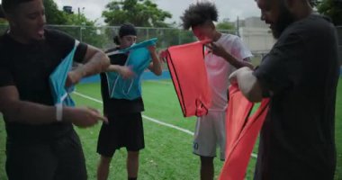 Hispanik arkadaşlar günlük futbol maçından önce renkli antrenman yelekleri giyiyorlar. Takımları hazırlıyorlar. Oyuncak enerji, kahkaha ve takım çalışması.