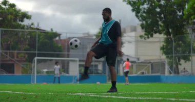Afrika kökenli futbol oyuncusu sahaya ayak basan top, şehir spor parkında ısınma antrenmanı sırasında kontrol ve çevikliği geliştirmek için tekmeler atıyor.