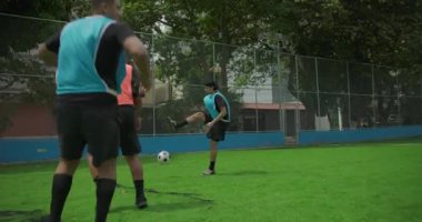 İki arkadaş mahalle sahasında futbol oynuyor, biri turuncu yelek giyiyor ve diğeri mavi, arkadaşça oyun sırasında pas veriyor, takım çalışması ve boş zaman aktivitesi kavramı.