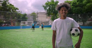 Kollarının altında futbol topuyla gururla duran, güneşli şehir sahasında gülümseyen, takım çalışmasının, pozitifliğin ve toplum atletizmine adanmışlığın sembolü olan Afrikalı Amerikalı Latin bir adam.